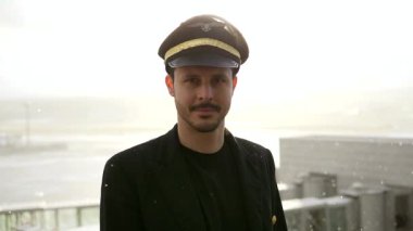 Genç erkek pilot, karlı havada havaalanında poz veriyor.
