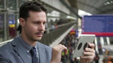 Genç beyaz adam tren istasyonunda tablet PC kullanıyor.
