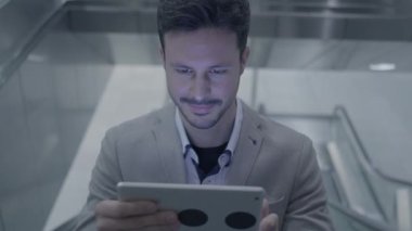 Genç beyaz adam asansörde tablet bilgisayar kullanıyor.
