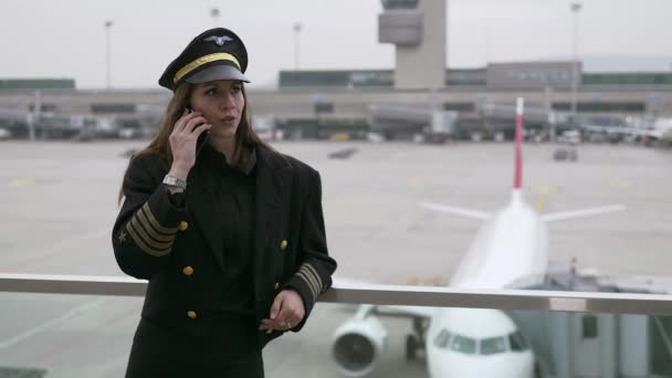 美しい女性パイロットは 空港で携帯電話で話しています — ストック動画