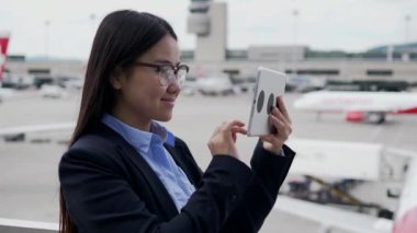 Genç mutlu Asyalı iş kadını havaalanında tablet kullanıyor. 