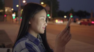Genç Asyalı kadın geceleri yol kenarında tablet kullanıyor.
