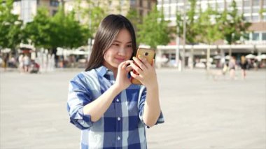 Genç Asyalı kadın şehir merkezinde dururken cep telefonu kullanıyor.