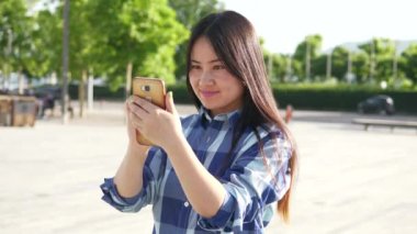Genç Asyalı kadın şehir merkezinde dururken cep telefonu kullanıyor.