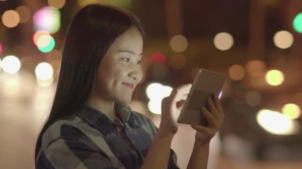 年轻的亚洲女人晚上在路旁用平板Pc — 图库视频影像