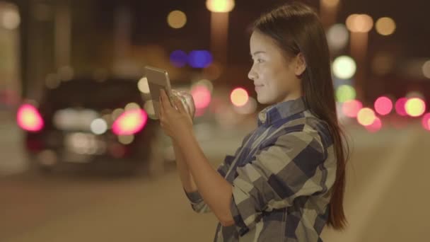年轻的亚洲女人晚上在路旁用平板Pc — 图库视频影像