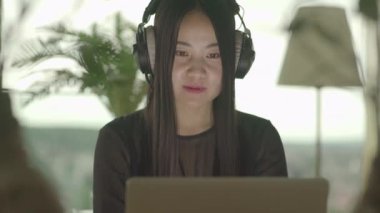 Genç Asyalı kadın evde dizüstü bilgisayarından müzik videosu izliyor.