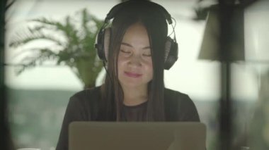 Genç Asyalı kadın evde dizüstü bilgisayarından müzik videosu izliyor.