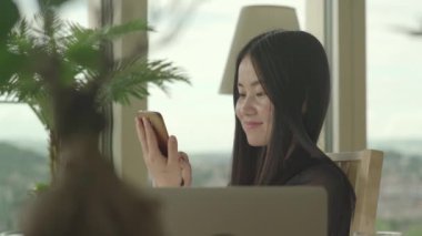 Genç Asyalı kadın evde cep telefonu kullanıyor.