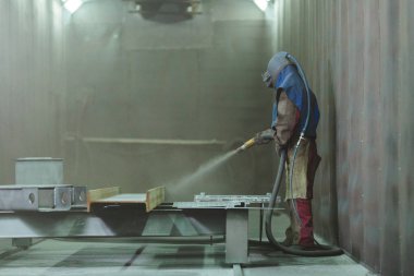 Kum püskürtme. Metal patlatma. Bir çalışanın bir metal parça boyama için hazırlar. Sert bir adam fabrikada çalışıyor.