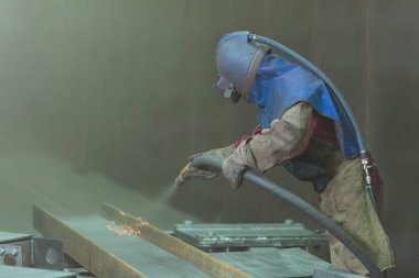 Kum püskürtme. Metal patlatma. Bir çalışanın bir metal parça boyama için hazırlar. Sert bir adam fabrikada çalışıyor.