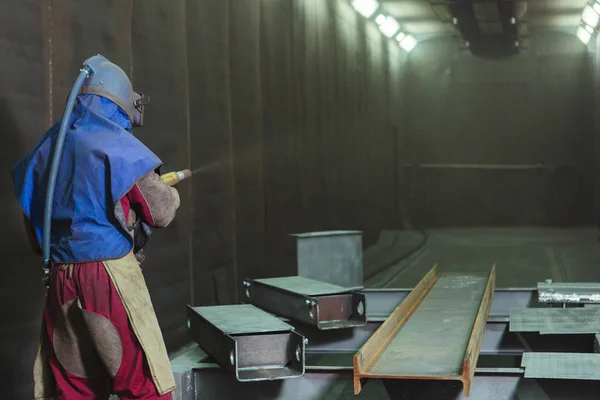 Kum püskürtme. Metal patlatma. Bir çalışanın bir metal parça boyama için hazırlar. Sert bir adam fabrikada çalışıyor.