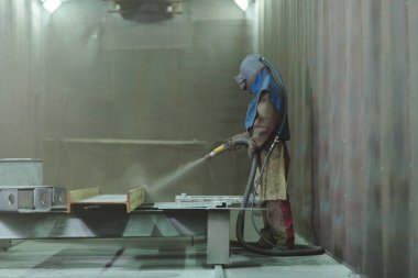 Sandblast. Blasting metal. An employee prepares a metal part for painting. A harsh man works in the factory. clipart
