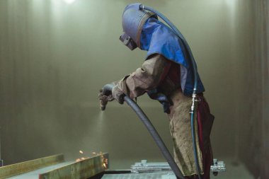 Kum püskürtme. Metal patlatma. Bir çalışanın bir metal parça boyama için hazırlar. Sert bir adam fabrikada çalışıyor.