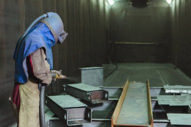 Kum püskürtme. Metal patlatma. Bir çalışanın bir metal parça boyama için hazırlar. Sert bir adam fabrikada çalışıyor.