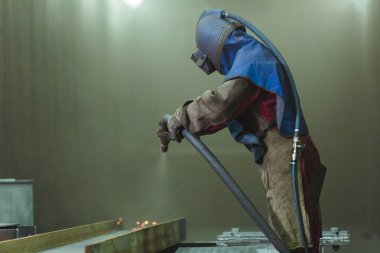 Kum püskürtme. Metal patlatma. Bir çalışanın bir metal parça boyama için hazırlar. Sert bir adam fabrikada çalışıyor.