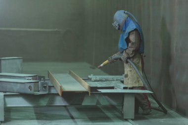 Kum püskürtme. Metal patlatma. Bir çalışanın bir metal parça boyama için hazırlar. Sert bir adam fabrikada çalışıyor.