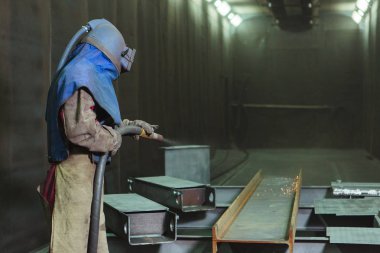 Kum püskürtme. Metal patlatma. Bir çalışanın bir metal parça boyama için hazırlar. Sert bir adam fabrikada çalışıyor.