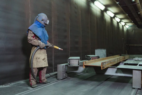 Kum püskürtme. Metal patlatma. Bir çalışanın bir metal parça boyama için hazırlar. Sert bir adam fabrikada çalışıyor.