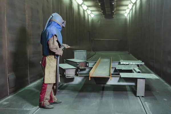 Kum püskürtme. Metal patlatma. Bir çalışanın bir metal parça boyama için hazırlar. Sert bir adam fabrikada çalışıyor.