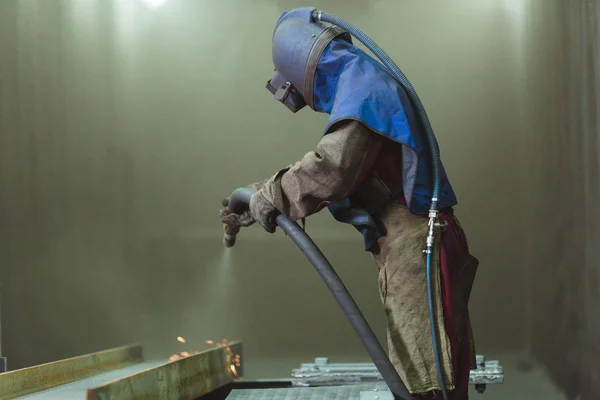 Kum püskürtme. Metal patlatma. Bir çalışanın bir metal parça boyama için hazırlar. Sert bir adam fabrikada çalışıyor.