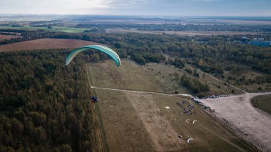 Yamaçparaşütü tarlalara uçar. Yüksek irtifa. Atlet termal geçerli döner. Yükselin. Hava uçuş için. Bir yol ile yeşil bir alan üzerinde uçan yamaçparaşütü üstten görünüm. Memnuniyeti.
