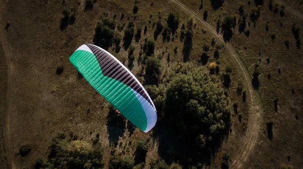 Paraglider flies over fields. High altitude. The athlete turns the thermal current. Rise up. Weather for flights. Top view of the paraglider flying over a green field with a road. Satisfaction. — Stock Photo, Image