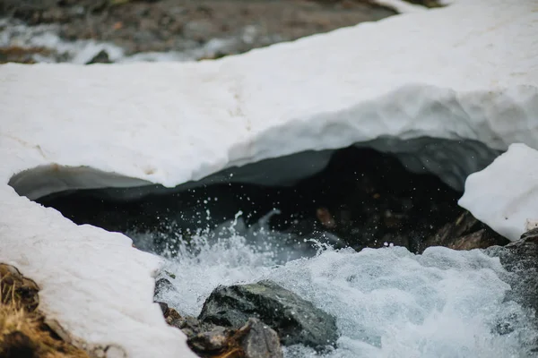 Le regard détaillé sur l'eau coule sous la glace dans une rivière. La neige fond des montagnes et coule dans le ruisseau, gros plan . — Photo