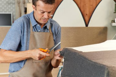 Qualified workman upholstering furniture in repair furniture workshop clipart