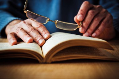 Yaşlı bir adam açık bir kitap ve gözlük eller
