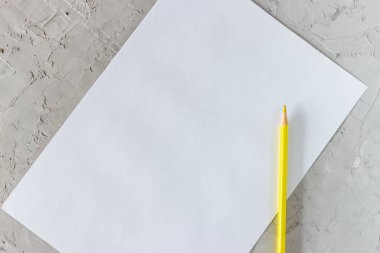 Sarı kalem ve gri beton arka planda beyaz kağıt.