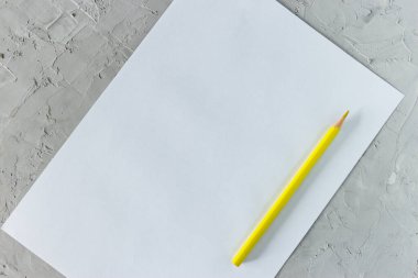 Sarı kalem ve gri beton arka planda beyaz kağıt.