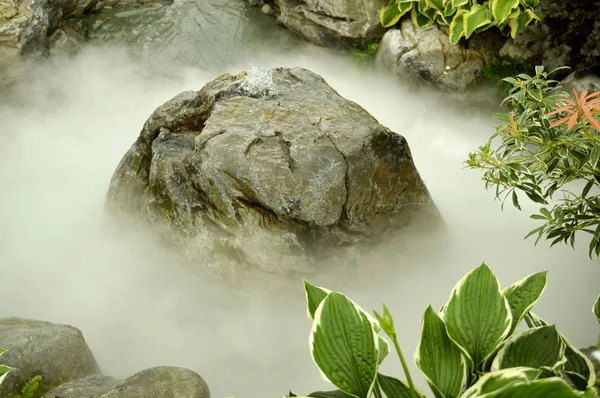 A fountain in a rocky water feature covered in mist