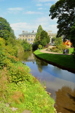 Tourists relaxing by the river in Buxton Pavilion Gardens clipart