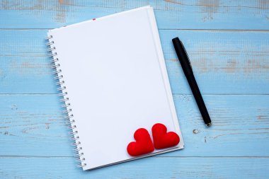 Aşktır... Defter ve kalem kelime çift kırmızı kalp şekli dekorasyon ahşap masa mavi arka plan ile. Düğün romantik ve Happy Valentine s gün tatil kavramı
