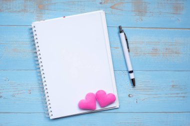 Blank notebook and pen with couple pink heart shape decoration on blue wooden table background. Wedding Romantic and Happy Valentine s day holiday concept