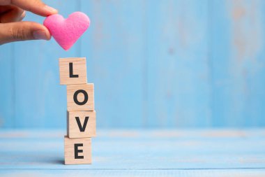 LOVE wooden cubes with pink heart shape decoration on blue table background and copy space for text. Love Romantic and Happy Valentines day holiday concept