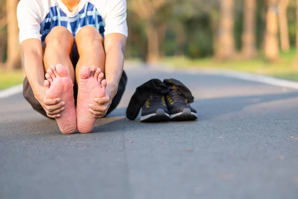 Young fitness man holding his sports leg injury. muscle painful during training. Asian runner having feet sole ache and problem after running and exercise outside morning. sport and healthy concepts