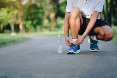 Parkta koşu ayakkabısı bağlayan genç bir atlet, erkek koşucu dışarıda yolda koşmaya hazır, Asyalı sporcu sabah yaya yolunda yürüyor ve egzersiz yapıyor. Refah ve spor kavramları