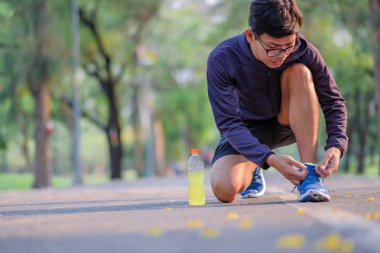 Parkta koşu ayakkabısı bağlayan genç bir atlet, erkek koşucu dışarıda yolda koşmaya hazır, Asyalı sporcu sabah yaya yolunda yürüyor ve egzersiz yapıyor. Refah ve spor kavramları