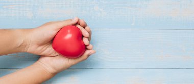 Mavi pastel renk ahşap arka plan üzerinde kırmızı kalp şekli tutan üstten görünüm el. Sağlık, organ bağışı ve sigorta veya sevgi ve Sevgililer günü kavramları