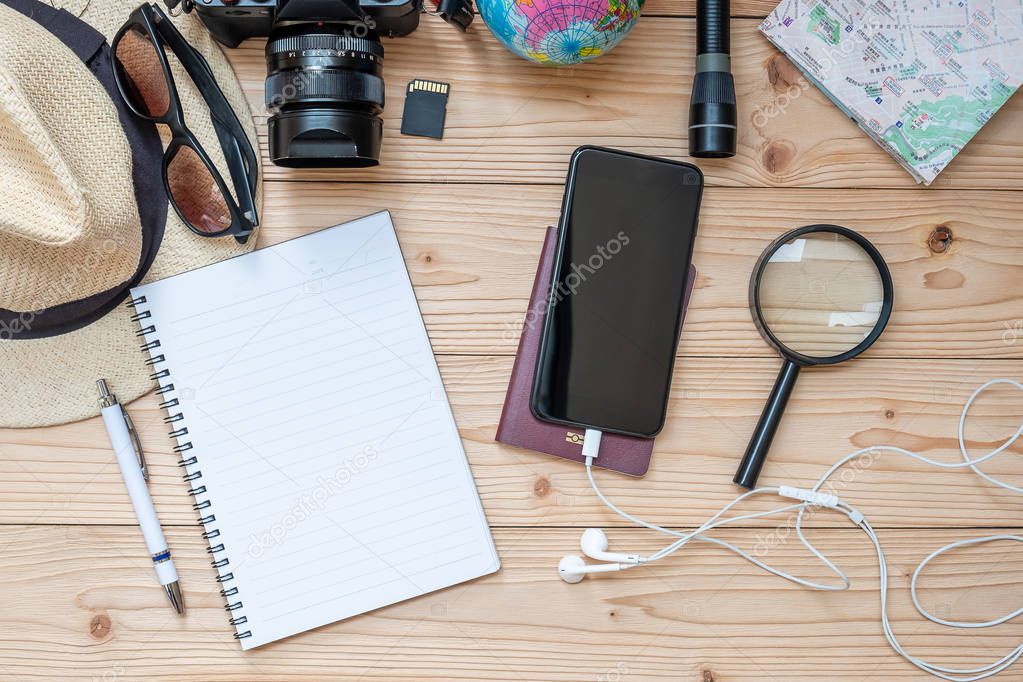 Travel planning concept background. Traveler's accessories; Map, Camera, Passport, Flashlight, Magnifying, smart Phone, Sunglasses, Hat and Notebook with Pen on wooden table, Top view and copy space