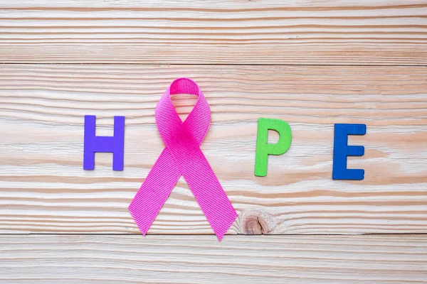 World cancer day (February 4) or Breast cancer, hope letter and pink ribbon on wooden background  for supporting people living and illness. Healthcare and medicine concept