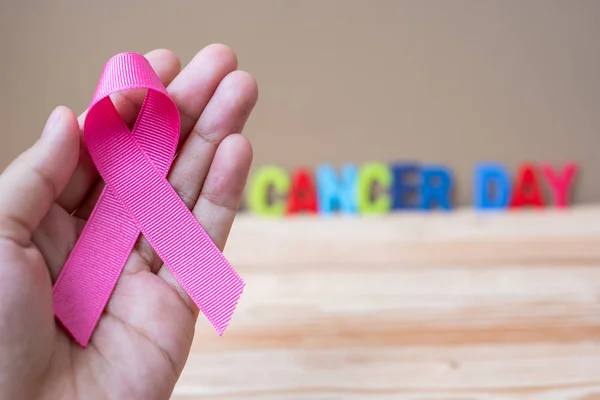 World cancer day (February 4) or Breast cancer,  pink ribbon on wooden background  for supporting people living and illness. Healthcare and medicine concept