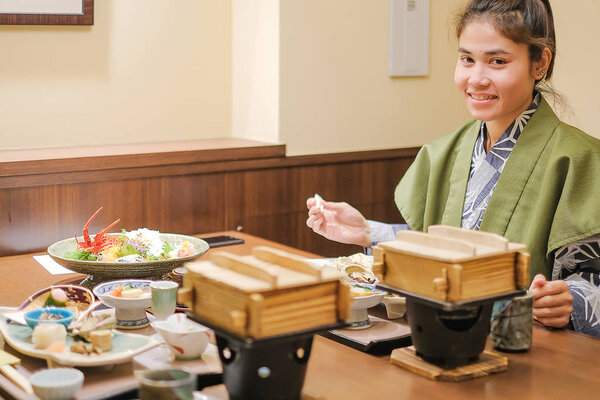 young Asian woman wearing Yukata with Japanese Dinner set and appetizer on wooden table in Traditional ryokan resort at Kawaguchiko lake, Yamanashi, Japan