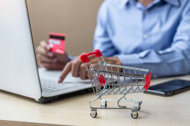 mini arabası, kredi kartı tutan ve siparişleri yaparken online alışveriş için dizüstü bilgisayar kullanarak Asya işadamı kapatın. Internet, teknoloji, e-ticaret ve online ödeme kavramı