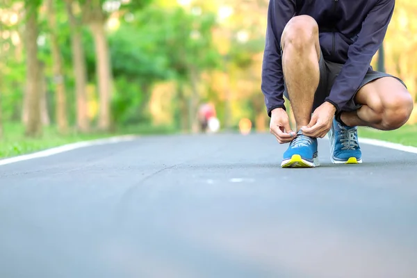Молодой спортсмен завязывает кроссовки в парке на открытом воздухе, мужчина — стоковое фото