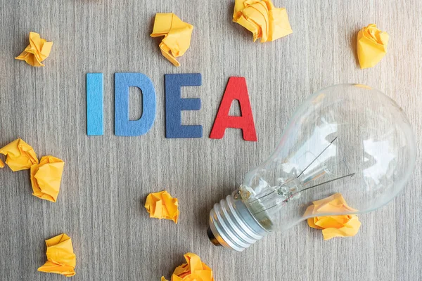 Idea TEXT on and crumbled paper with lightbulb on wooden table b — Stock Photo, Image