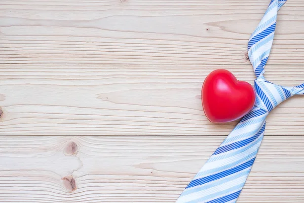 blue necktie and red heart shape on wooden background with copy