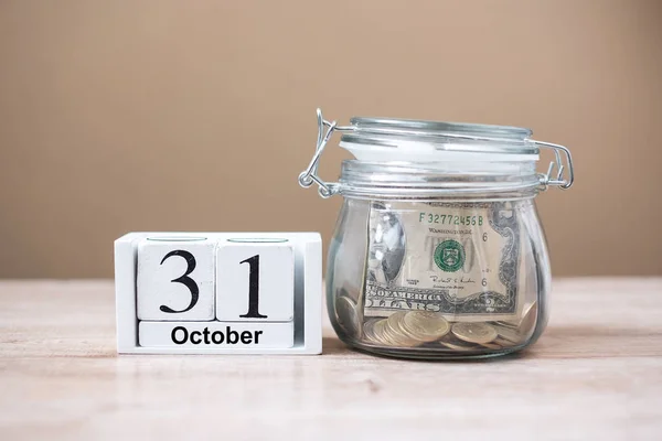 31 октября календарь деревянный и деньги в стеклянной банке на столе, w — стоковое фото